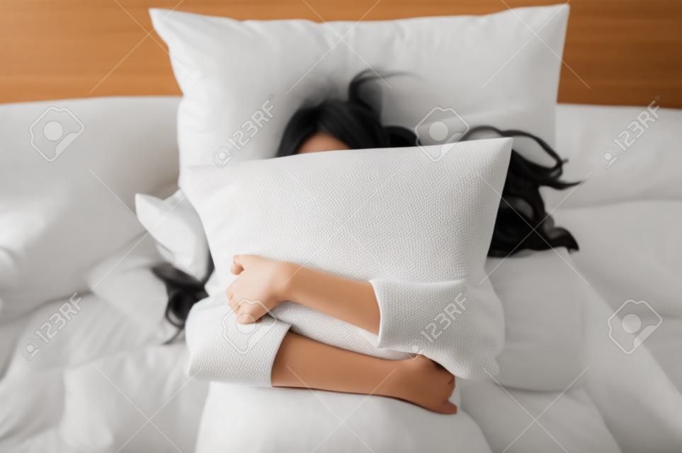 Una joven asiática feliz abraza la almohada en la cama por la mañana