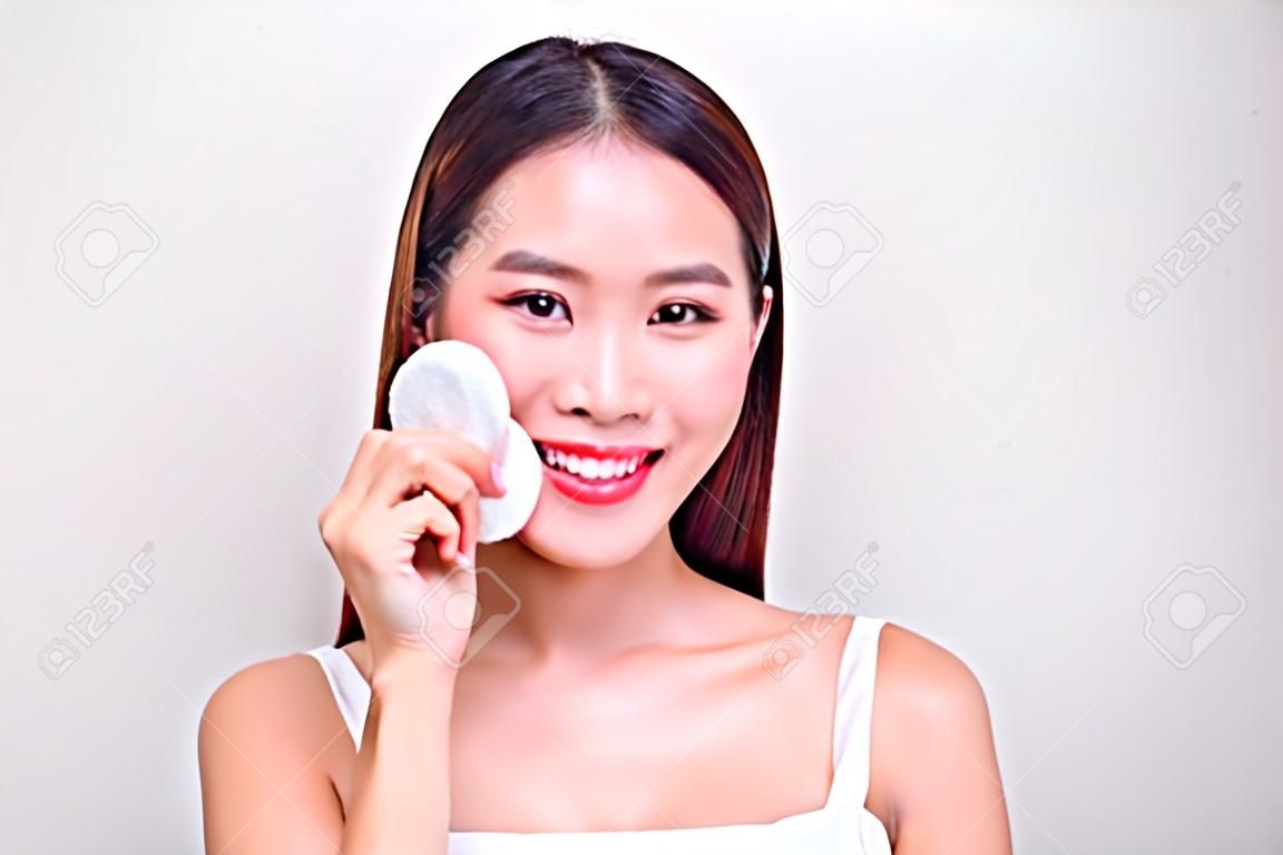 由化裝棉的愉快的微笑的美麗的年輕亞洲婦女清潔皮膚。
