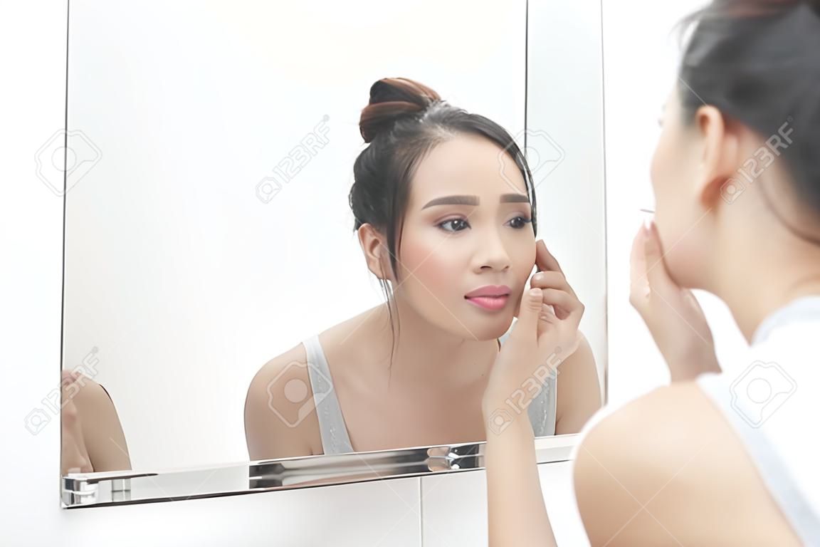 Skin care. Woman applying skin cream on her face in front of mirror
