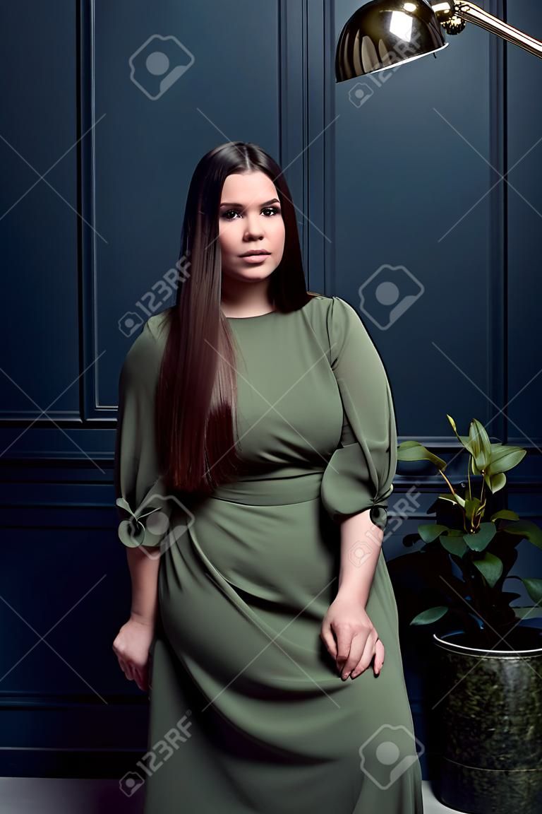 Beautiful happy young female brunette with straight hair in a studio setting while wearing a green dress on a dark blue background