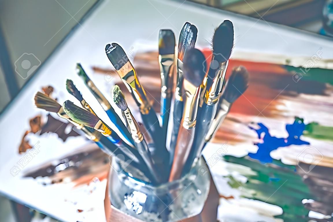 Pinsel zum Zeichnen stehen in einem Glas mit einer Borste nach oben in einem Bild aus Abstrichen mit Ölfarben.