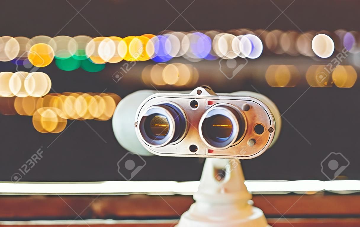 Touristic telescope look at city with view of Barcelona Spain, close up old metal binoculars on background viewpoint, hipster coin operated in panorama observation, mockup flare, illumination bokeh light in night blur atmospheric sky