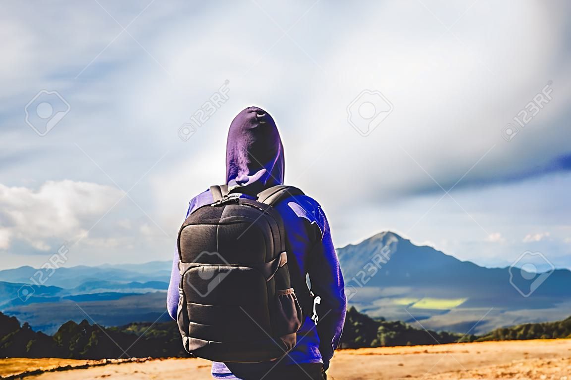 Touristischer Reisender mit schwarzem Rucksack auf dem Gipfel des Berges im Hintergrund, Reisender schaut auf blaue Himmelswolken, Wanderer, der die Naturpanoramalandschaft auf der Reise genießt, entspanntes Urlaubsmodellkonzept auf der Trekkingreise