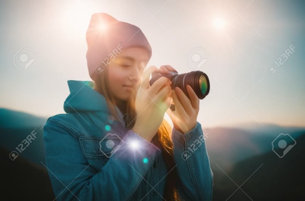 hipster tourist girl hold in hands take photography click on modern photo camera, photographer look on camera technology, journey landscape vacation concept, sun flare mountain