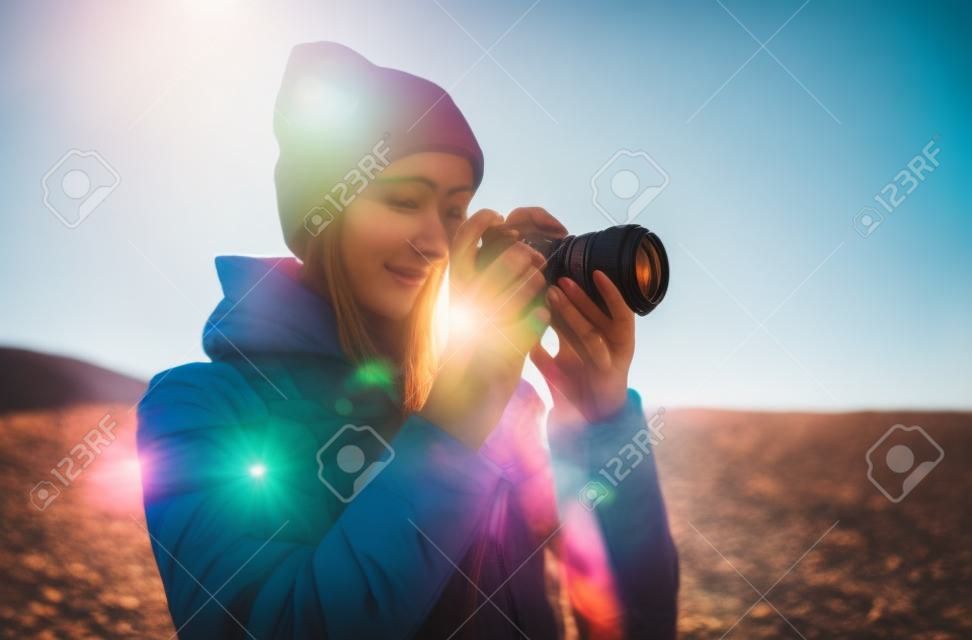 Chica turista hipster sostenida en las manos, toma fotografía, haz clic en una cámara fotográfica moderna, mira el fotógrafo en la tecnología de la cámara, concepto de vacaciones en el paisaje del viaje, montaña de bengalas solares