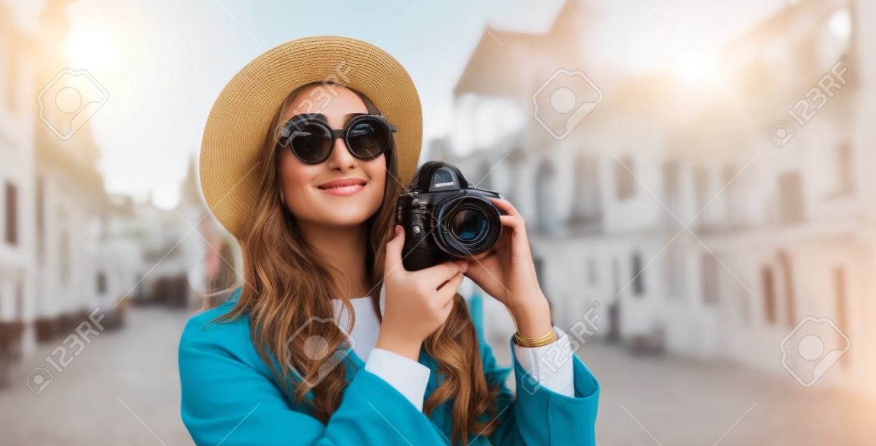 Hobby photographer concept. Outdoor lifestyle portrait of pretty woman in sun city in Europe with camera travel photo of photographer in glasses and hat take photo copy space mockup