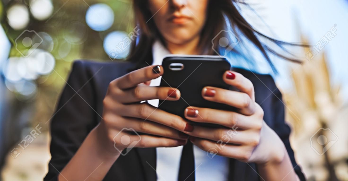 Piękna młoda kobieta biznesu patrząca na smartfon na zewnątrz z bliska na ręce dziewczyny, która pisze wiadomość w pustym miejscu na telefon komórkowy