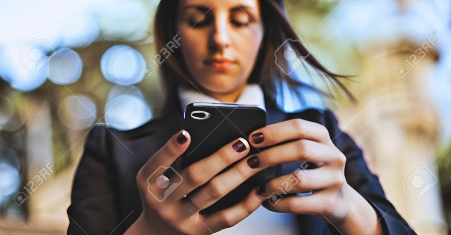 야외에서 스마트 폰을 찾고 아름 다운 젊은 비즈니스 우먼. 휴대폰에 메시지를 쓰는 소녀의 손 클로즈업, 텍스트를 위한 빈 공간