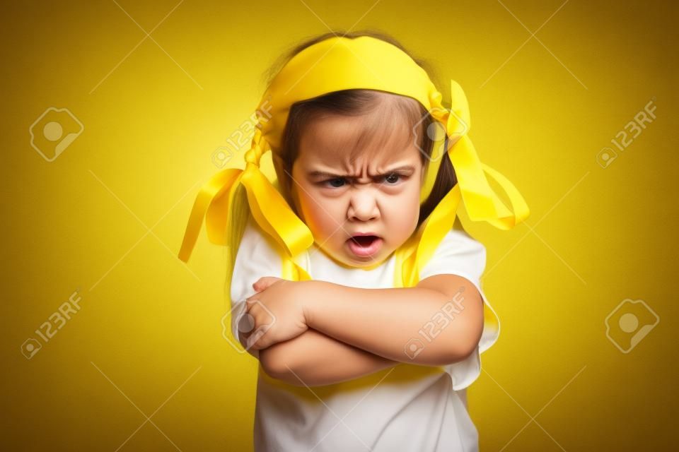 Angry little girl with yellow bows and yellow T-shirt over white background, sign and gesture concept