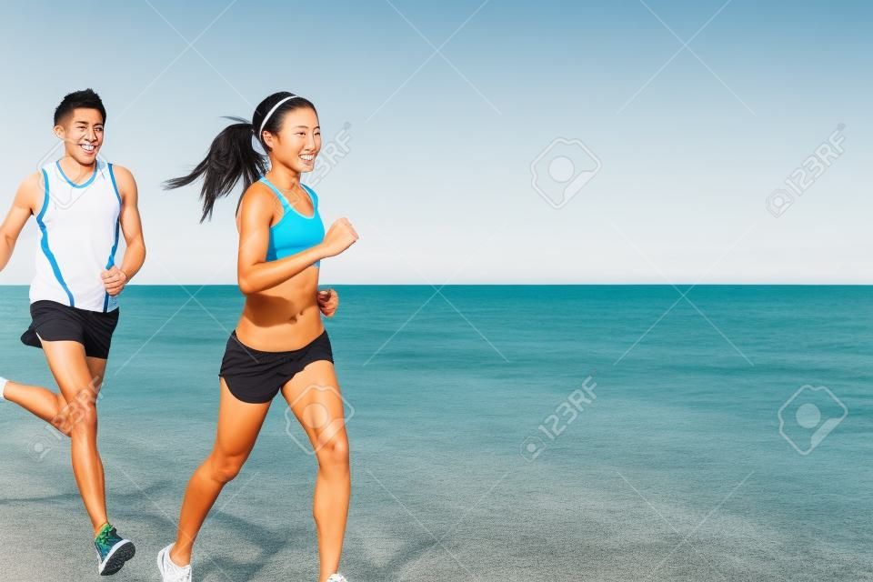 運動 - 夫婦海灘上運行馬拉松跑訓練探索。年輕的多種族的情侶選手，面帶微笑的亞洲女性健身模型和高加索的男模。