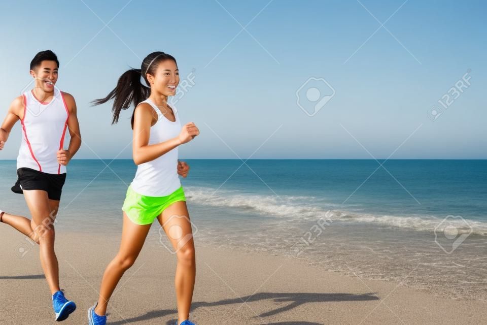 運動 - 夫婦海灘上運行馬拉松跑訓練探索。年輕的多種族的情侶選手，面帶微笑的亞洲女性健身模型和高加索的男模。