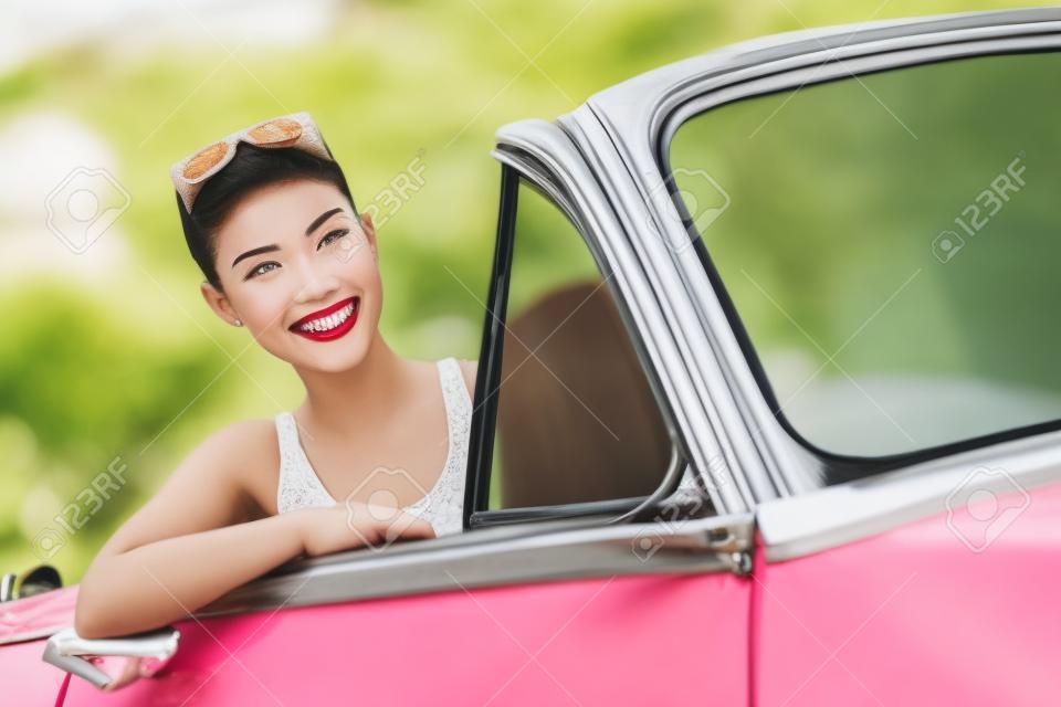 Woman Driving Oldtimer. Retro-Stil Bild der glücklich lächelnde junge Frau in rosa alten Auto, das auf Road Trip an sonnigen Frühlings-oder Sommertag. Schöne multirassischen Kaukasier / chinesische asiatische Lifestyle-Modell im Freien. Szenenfoto aus Havanna, Kuba.