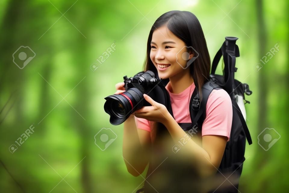 Nature travel photographer woman taking pictures in forest during hiking trip. Beautiful happy smiling young woman holding professional SLR camera. Mixed race Chinese Asian / Caucasian girl photographing