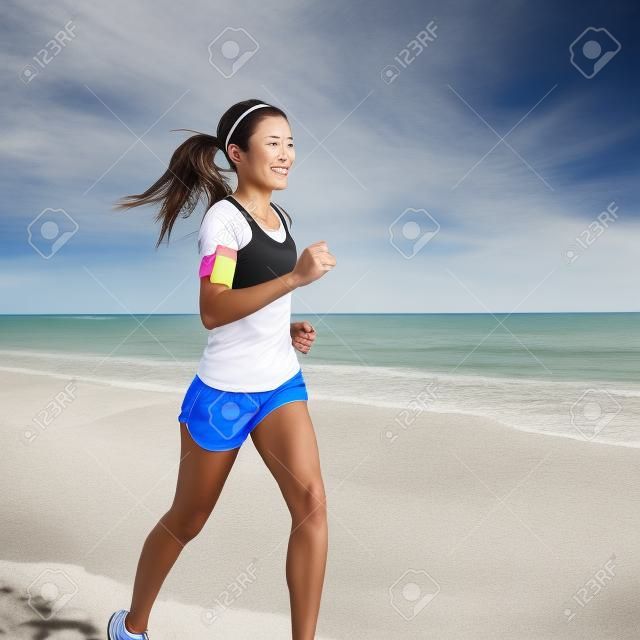 Ejecución de mujer corriendo en la playa escuchando música en los auriculares del teléfono elegante reproductor de mp3 brazalete smartphone, formación Mujeres corredor de maratón en la hermosa playa. Mixed mujer asiática raza.