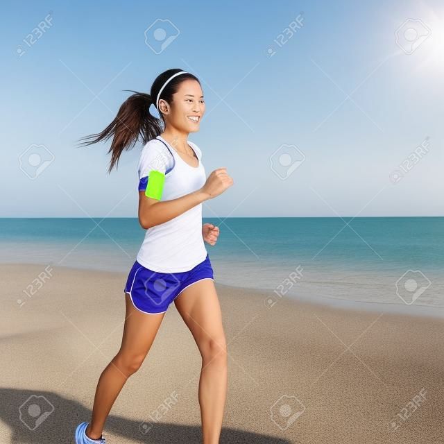 Laufende Frau Joggen am Strand Musik hören in Kopfhörer von MP3-Player Smartphone Smartphone Armbinde, Läuferin Training für Marathon am schönen Strand. Mixed Rennen asiatischen Frau.