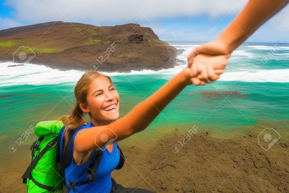 Mano amiga - excursionista mujer recibiendo ayuda en caminata sonriendo feliz superando obstáculo. Mochileros turísticos caminando en la playa de arena verde, Papakolea en Big Island, Hawaii, Estados Unidos. Pareja joven viajando.