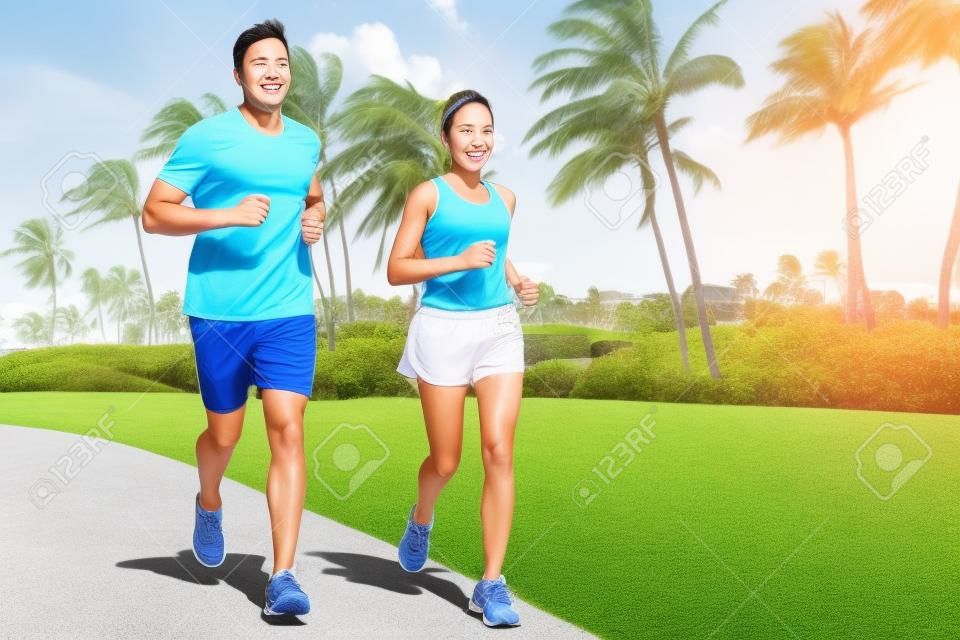 スポーツ カップルを行使夏の路上外走破。幸せなアクティブな若い大人の都市公園やリゾート道路で熱帯背景と一緒にジョギング フィットします。アジアと白人の人々。