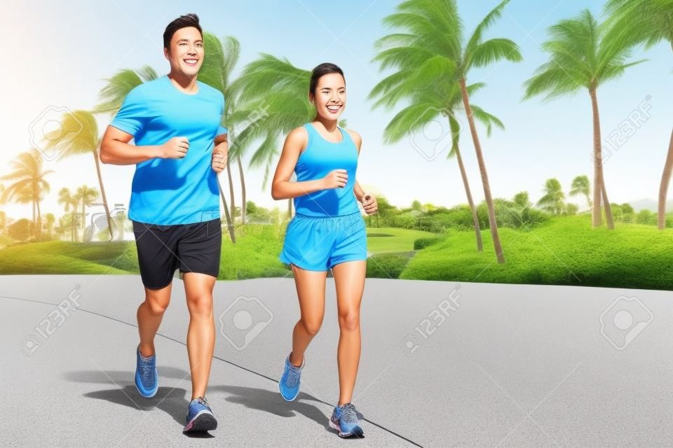 Sport couple exercising running outside on street in summer. Happy active young fit adults jogging together with tropical background in city park or resort road. Asian and Caucasian people.