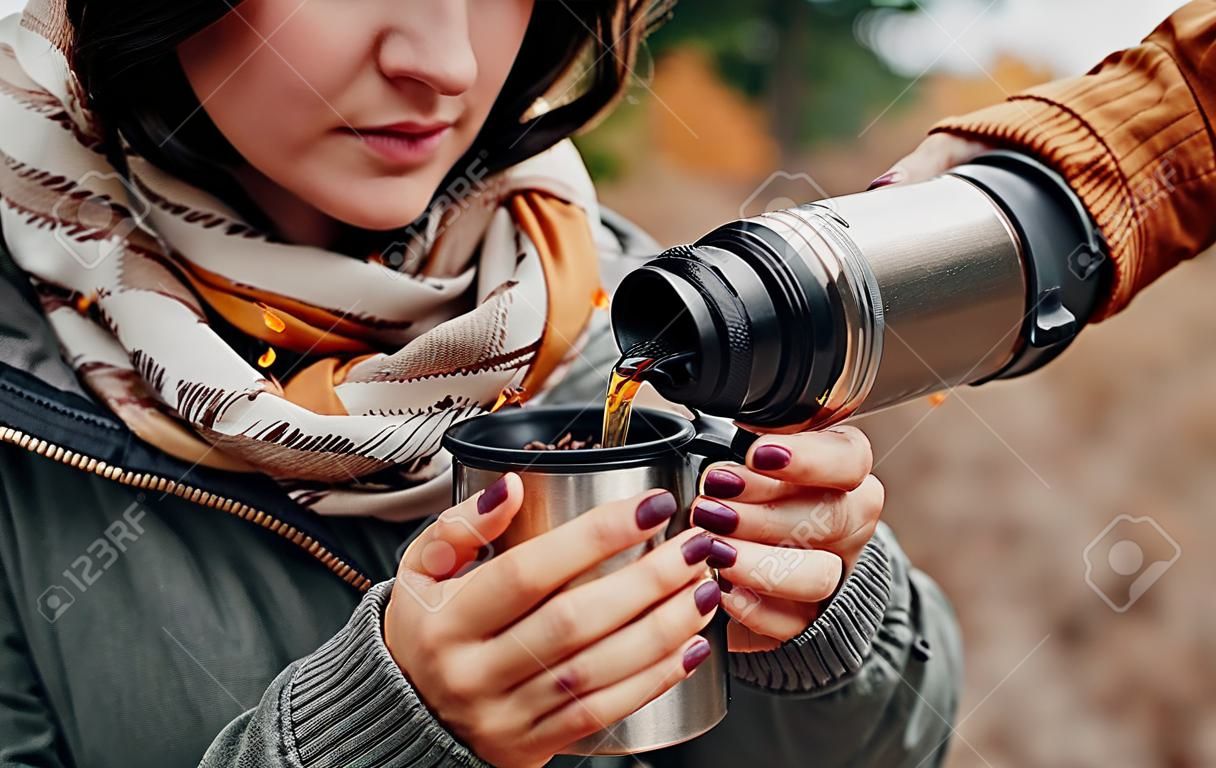 Man pours hot tea out of bottle for his girlfriend in autumn forest