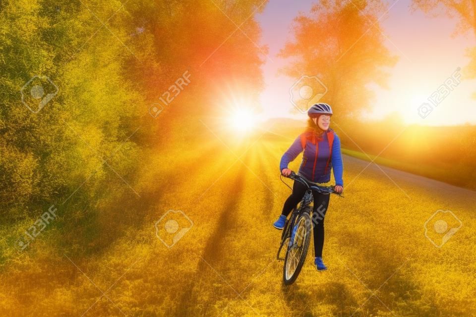 Young bicyclist riding in autumn field at sunset. Happy woman smiling. Active way of life