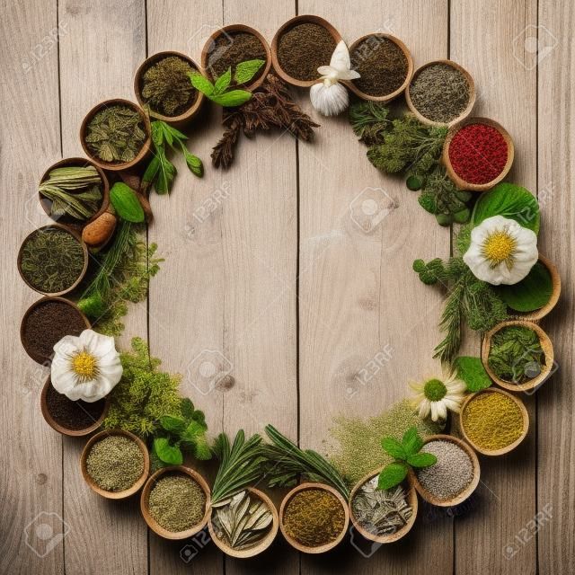 Seleção natural de flores e ervas usadas na medicina herbal em tigelas e soltas formando um círculo sobre fundo de madeira angustiado.