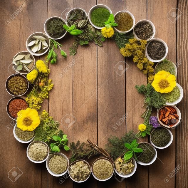 Seleção natural de flores e ervas usadas na medicina herbal em tigelas e soltas formando um círculo sobre fundo de madeira angustiado.