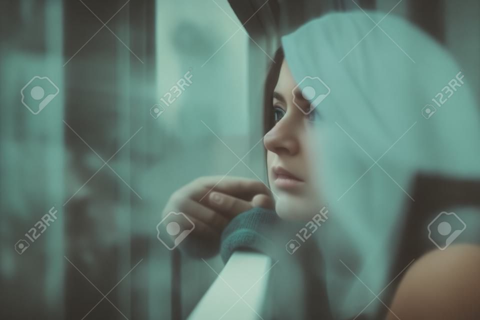 Młoda smutna kobieta patrząca na zewnątrz przez balkon budynku mieszkalnego
