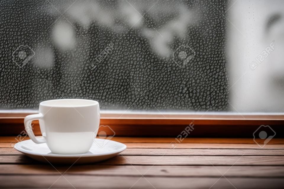 뜨거운 차 또는 빈티지 나무 창턱 또는 흐린 배경에 빗방울이 창에 대 한 테이블에 커피의 잔을 김이 흰색. 얕은 포커스.