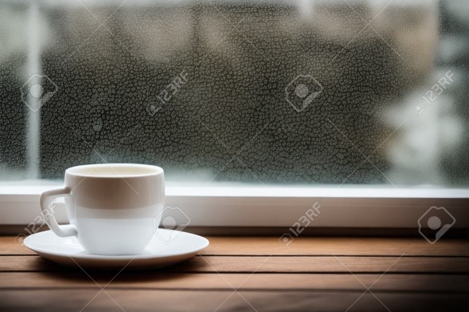 뜨거운 차 또는 빈티지 나무 창턱 또는 흐린 배경에 빗방울이 창에 대 한 테이블에 커피의 잔을 김이 흰색. 얕은 포커스.
