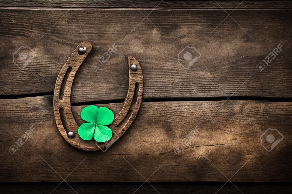Old horseshoe and four leaf clover on a vintage wooden board. The concept of luck, luck, luck. St. Patricks Day card.