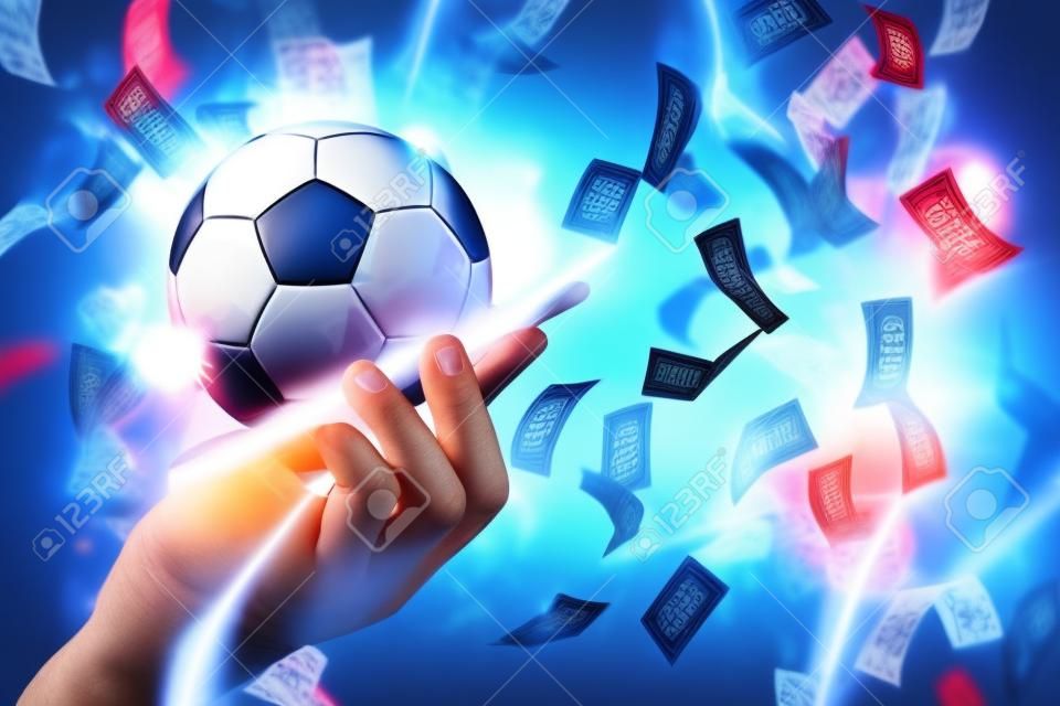 Online-Sportwetten. Dollar fallen auf den Hintergrund einer Hand mit einem Smartphone und einem Fußball. Kreativer Hintergrund, Glücksspiel