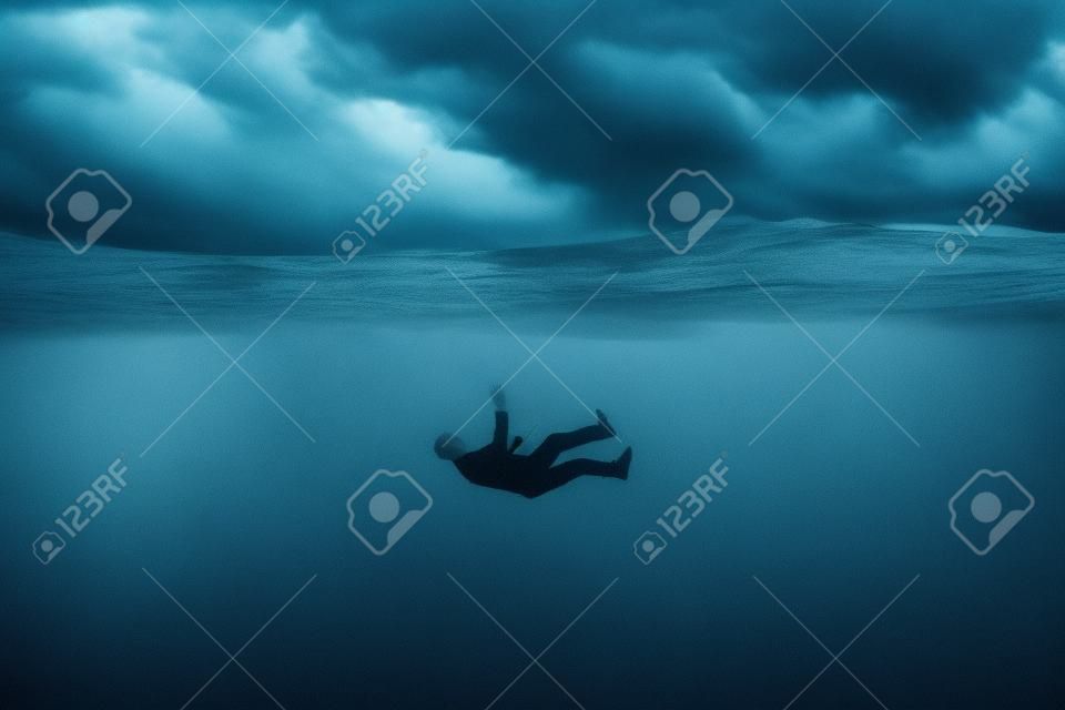 Der menschliche Körper versinkt in grauem Wasser, sinkt auf den Grund, graue Wolken. Depression, Aufschub, Verzweiflung, Angst, Apathie