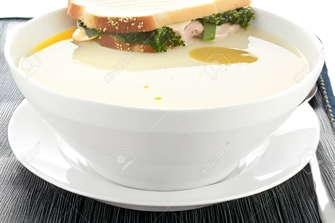Un tazón de sopa de pollo con un sándwich de atún