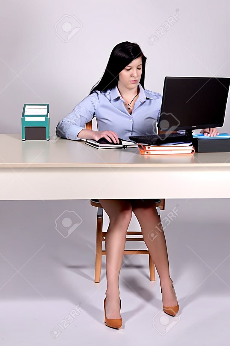 Mujer joven que trabaja detrás de una recepcionista en el ordenador portátil con las piernas en forma de A