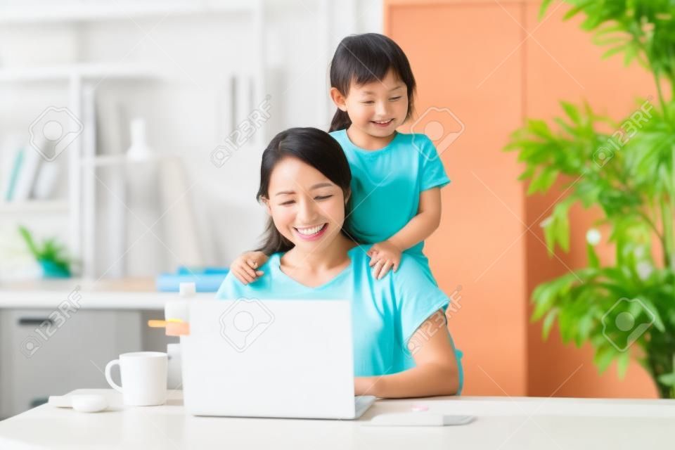 Azjatycka kobieta robi telepracę w pokoju domowym podczas zabawy z córką
