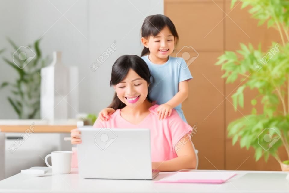 Azjatycka kobieta robi telepracę w pokoju domowym podczas zabawy z córką