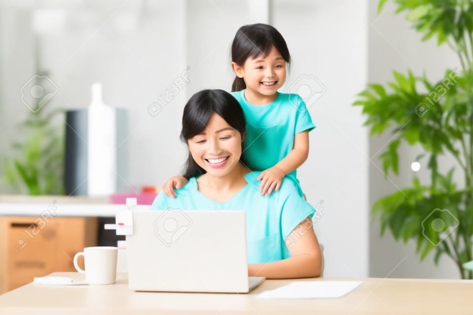 Asian woman doing telework in home room while playing with her daughter