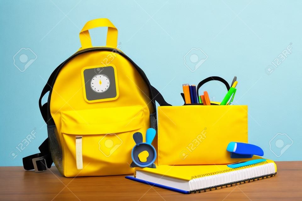 Powrót do składu szkoły, koncepcja edukacji. żółty plecak z przyborami szkolnymi - notatnik, długopisy, zszywacz, ołówek, temperówka izolowane na niebieskim tle makieta transparentu.