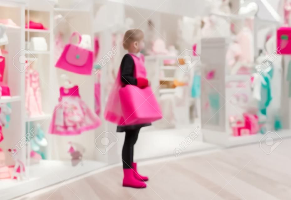 Offuscata giovane donna guardando una finestra luminosa di un nuovo boutique di lusso per bambini abbigliamento e accessori. Grandi vendite di Black Friday per Natale