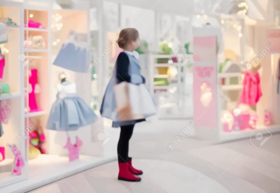 Offuscata giovane donna guardando una finestra luminosa di un nuovo boutique di lusso per bambini abbigliamento e accessori. Grandi vendite di Black Friday per Natale