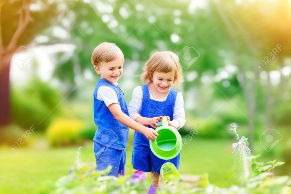 Lindo niño y niña regando plantas en el jardín en un día soleado de verano. Mami pequeños ayudantes. Hermano y hermana jugando juntos