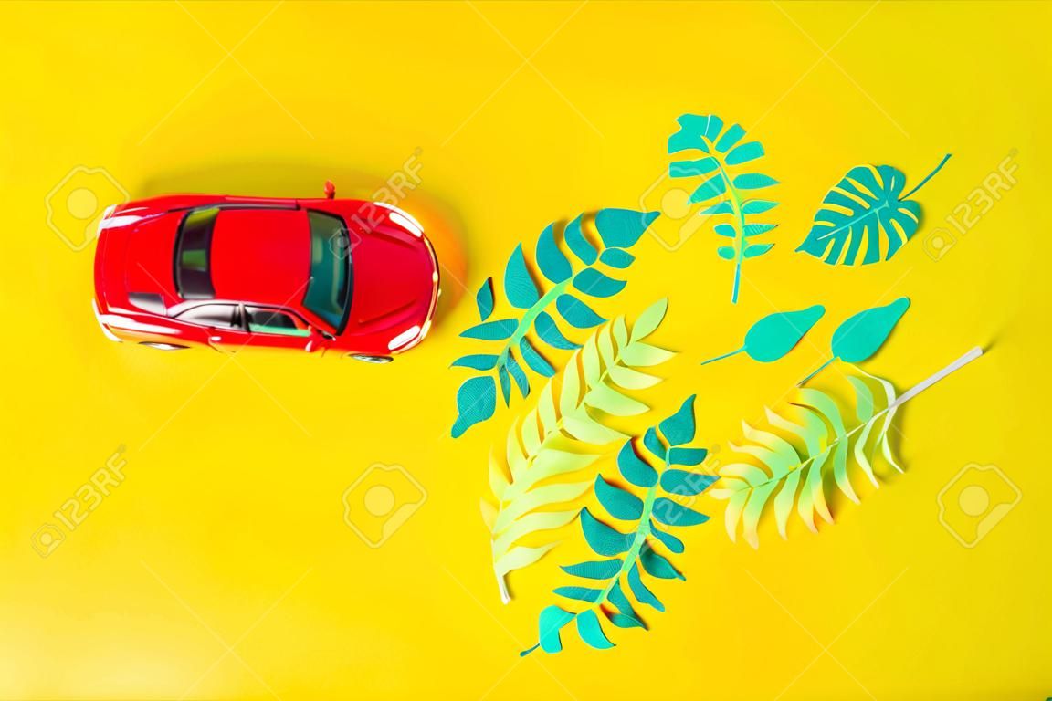 kleine speelgoed rode auto draagt tropische bladeren gesneden uit papier. Het concept van zomer en reizen