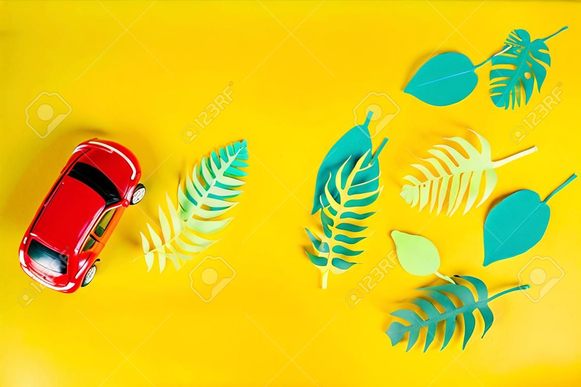kleine speelgoed rode auto draagt tropische bladeren gesneden uit papier. Het concept van zomer en reizen