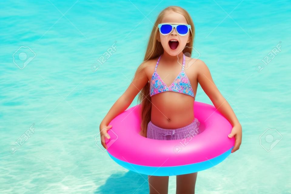 child with sunglasses and inflatable ring at the beach