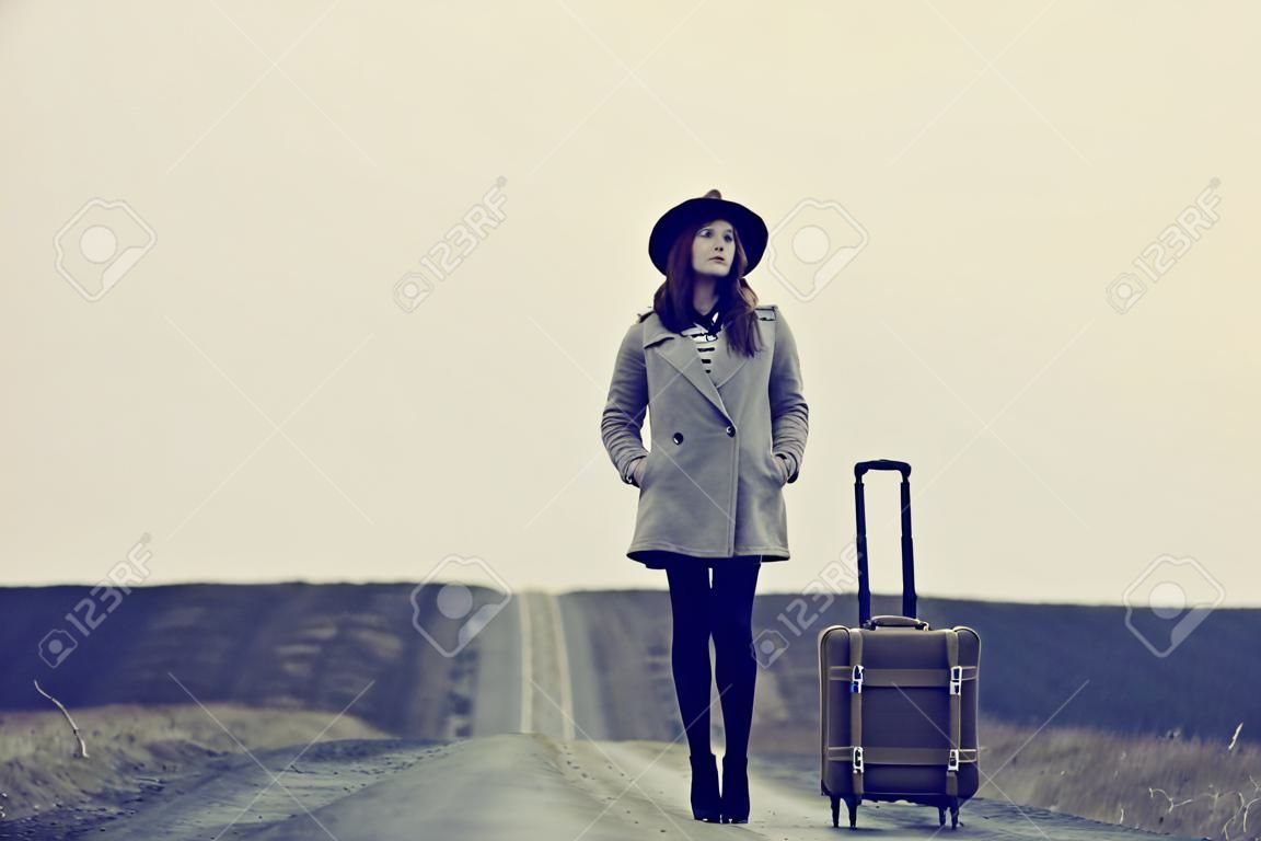 portrait of a young beautiful woman with suitcase standing on the road