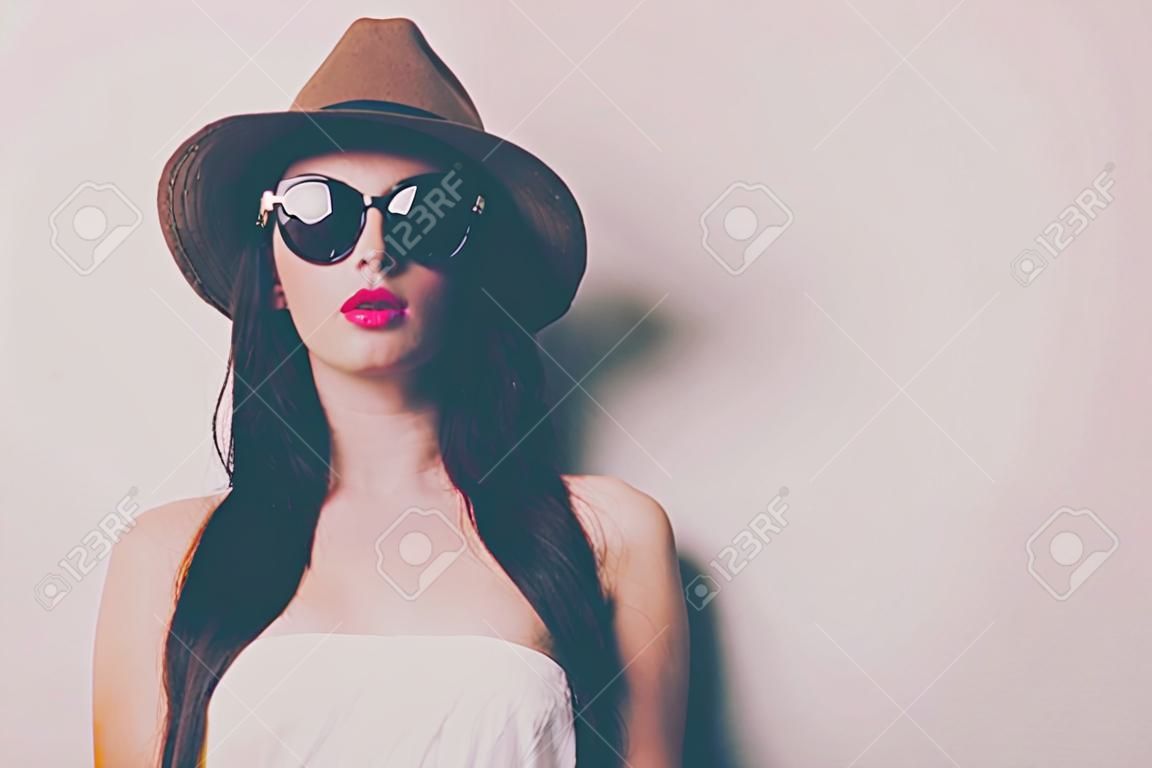 ritratto di giovane donna con occhiali da sole e cappello su sfondo bianco