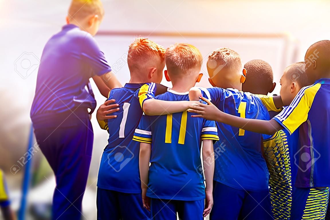 Kids sport team having pep talk with coach. Children soccer team motivated by trainer. Coaching football youth team. Young boys standing together united