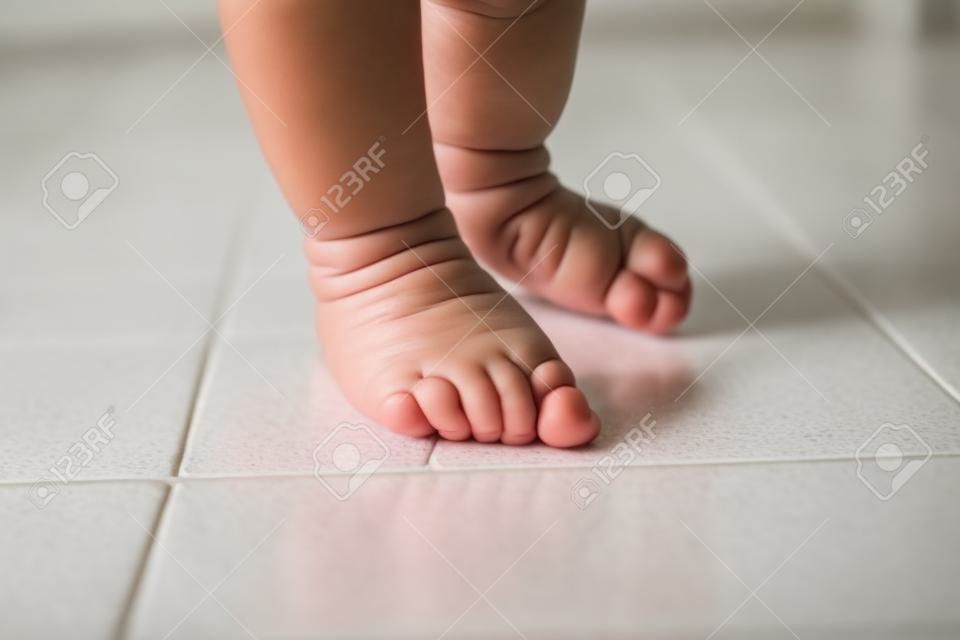 close-up of a latina baby girl's feet learning to walk on a white tile floor. taking her first steps.