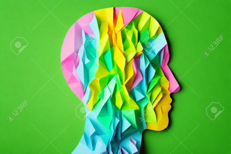 Head silhouette made of paper. Crumpled pink paper shaped as a human head with copy space on green and yellow paper background. Minimal concept.