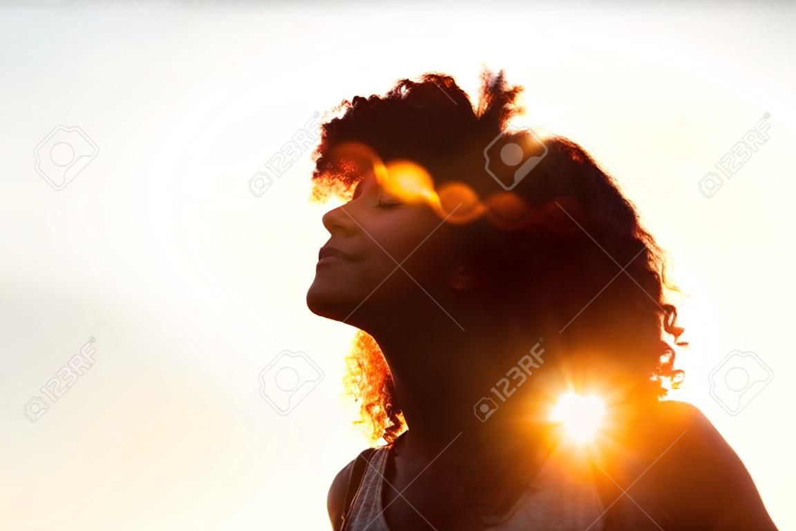 Profiel protrait van een mooie vrouw met afro stijl haar silhoueted tegen gouden zonnevlam op een zomeravond